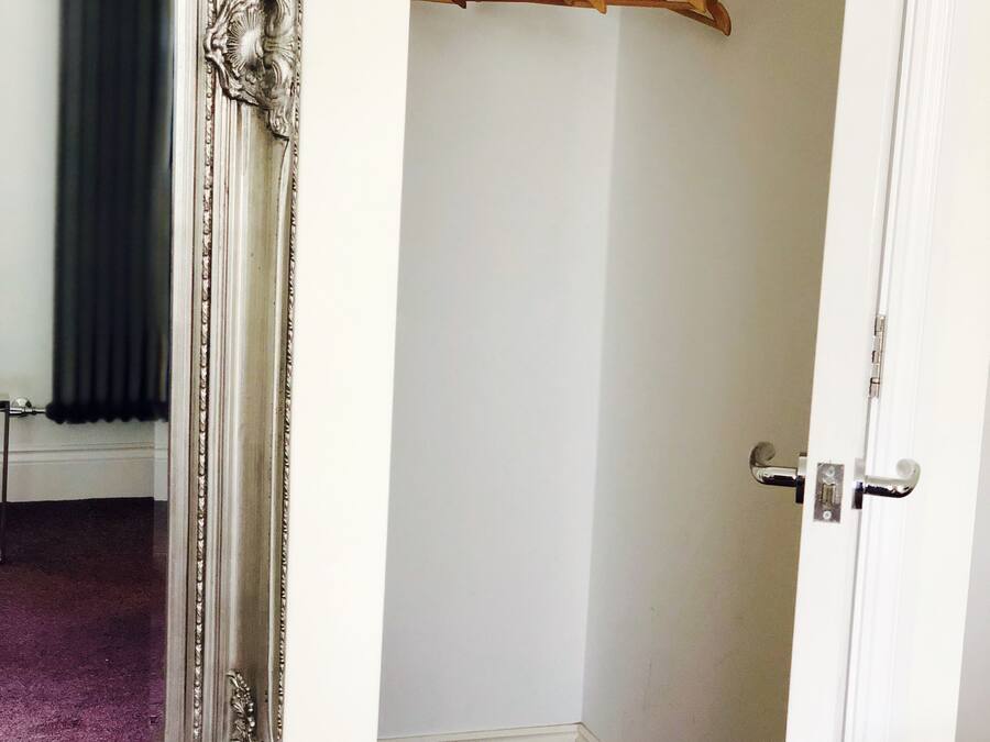 A room with a white door, a mirror with an ornate frame, and a wooden coat rack.