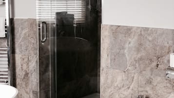 A modern bathroom with a glass-enclosed shower, a pedestal sink, and marble flooring.