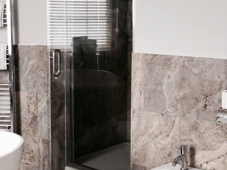 A modern bathroom with a glass-enclosed shower, a pedestal sink, and marble flooring.