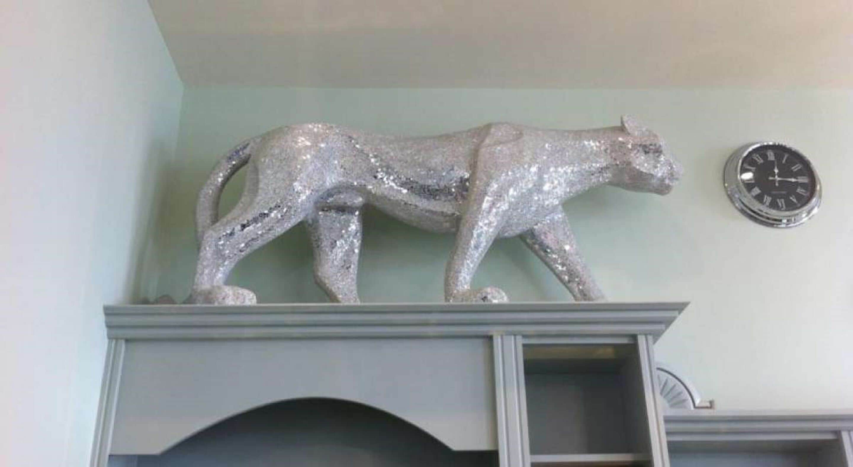 A silver cat sculpture on a mantelpiece above a fireplace.