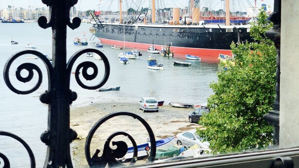 Een groot schip ligt aangemeerd in een haven, met kleinere boten in de buurt.