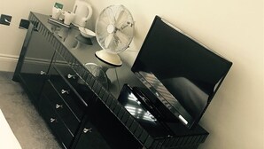 Een moderne hotelkamer met een zwarte dressoir, een flatscreen televisie, een ventilator en een koffiezetapparaat.