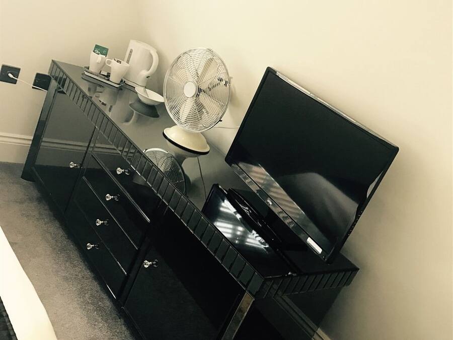 Een moderne hotelkamer met een zwarte dressoir, een flatscreen televisie, een ventilator en een koffiezetapparaat.