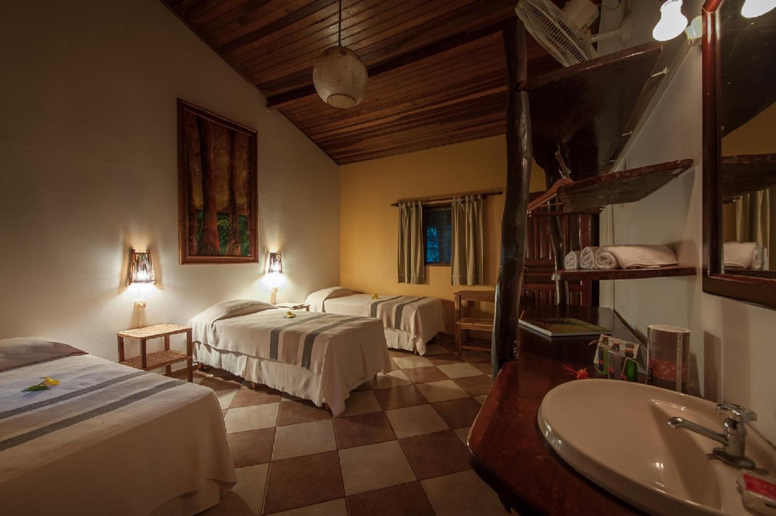 Une chambre d’hôtel avec deux lits, un grand miroir, un lavabo et un plafond en bois.