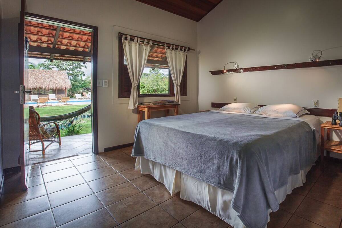 Un dormitorio con una cama, una mesita de noche, un estante de madera y vistas a un jardín por la ventana.