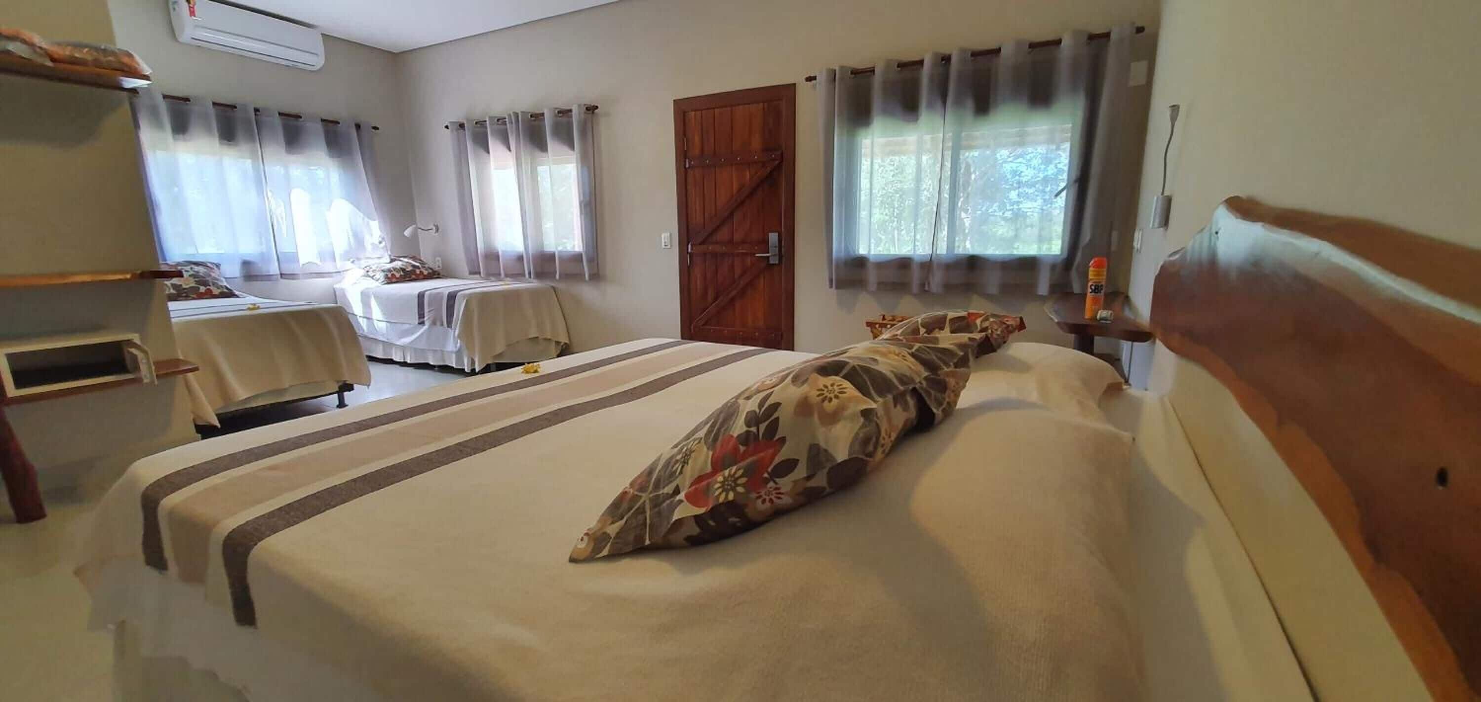 A hotel room with two beds, a wooden wardrobe, a desk with a chair, and a window with curtains.