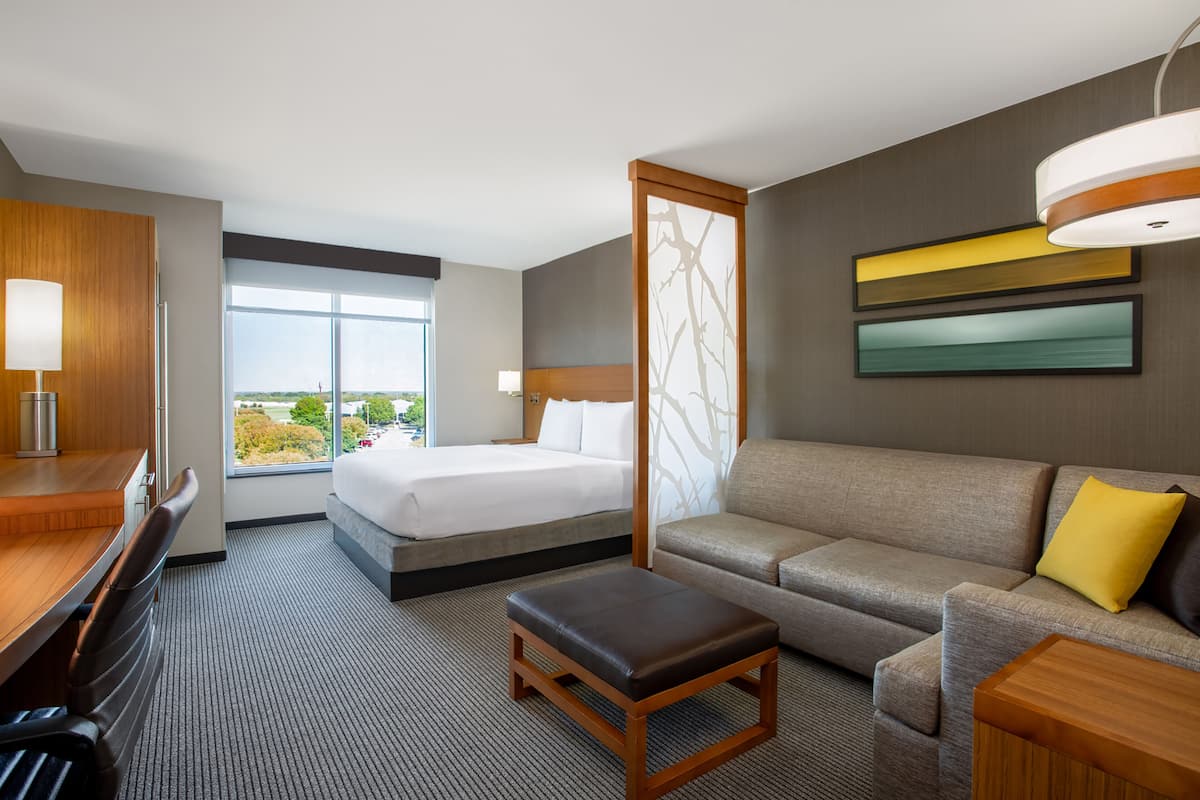 Habitación de hotel con cama, sofá, escritorio y vistas al exterior.