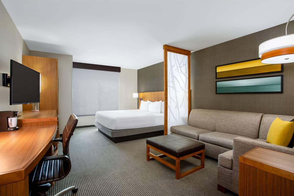 Una habitación de hotel con un escritorio de madera, una cama, un sofá y una televisión.