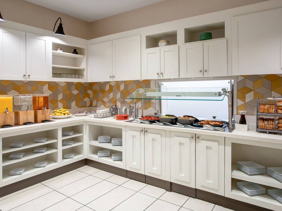 A modern kitchen with white cabinets, a glass water dispenser, and neatly arranged food items.