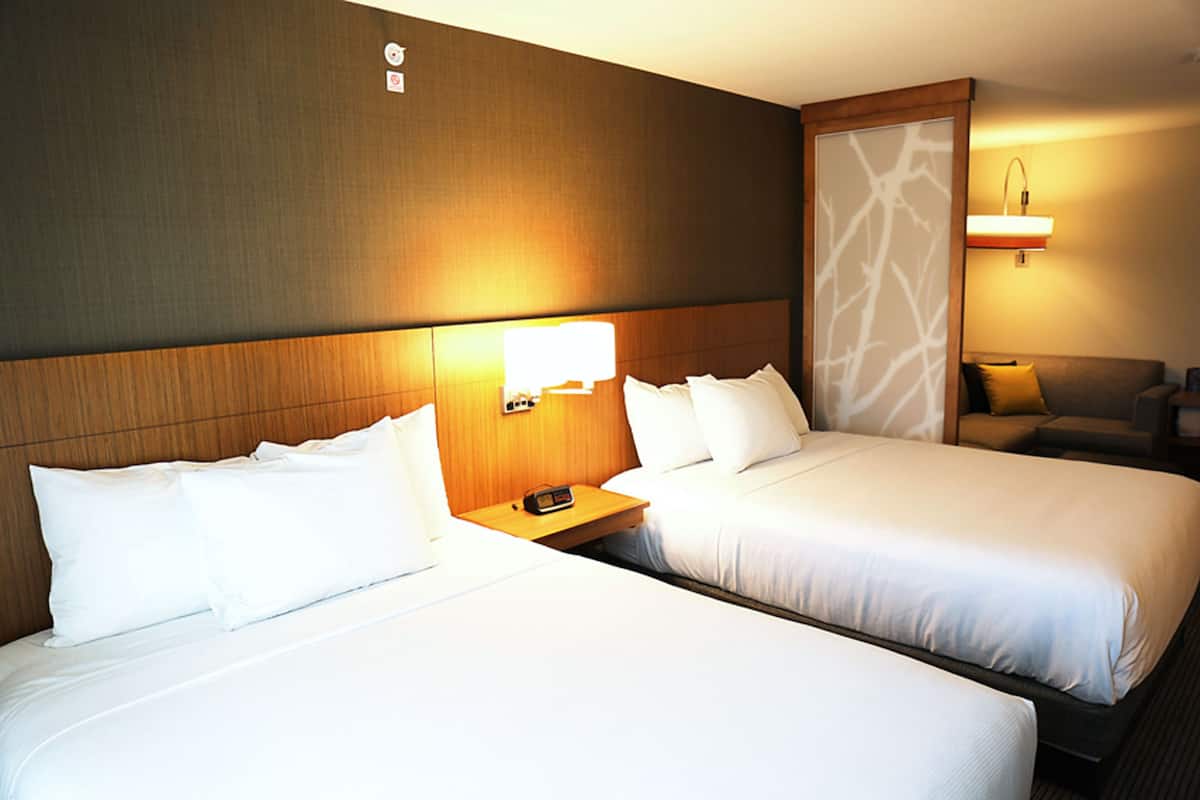 Una habitación de hotel con dos camas individuales, una mesita de noche con lámpara y un sofá.