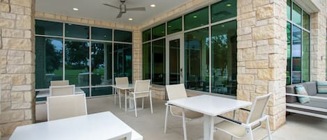 An outdoor patio area with stone walls, large windows, and white furniture.