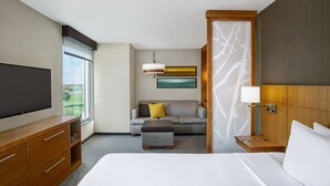 A hotel room with a large bed, a sofa, a TV, a wooden nightstand, and a window with a view. - Hyatt Place Austin Airport (Austin)