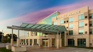 A modern hotel entrance with a covered walkway, large windows, and a clear sky. - Hyatt Place Austin Airport (Austin)