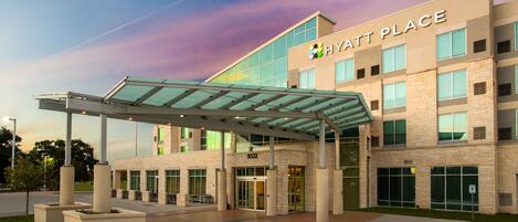 A modern hotel entrance with a covered walkway, large windows, and a clear sky.