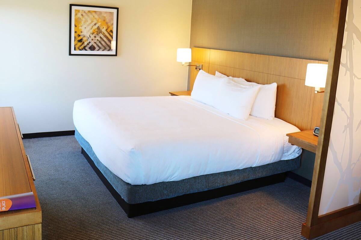 A hotel room with a large bed, two bedside lamps, a framed abstract artwork on the wall, and a wooden nightstand.