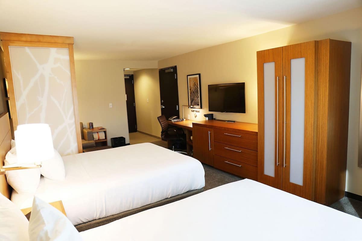 A hotel room with two beds, a desk with a chair, a television, and a wardrobe.