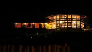 A building with a circular structure and a rectangular extension, illuminated at night.
