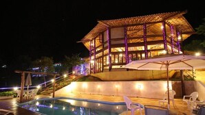 A poolside area with a wooden deck, lounge chairs, and a pool.