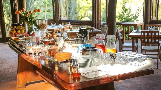 A breakfast buffet with various food items and beverages, set in a spacious outdoor dining area with natural light and greenery in the background.