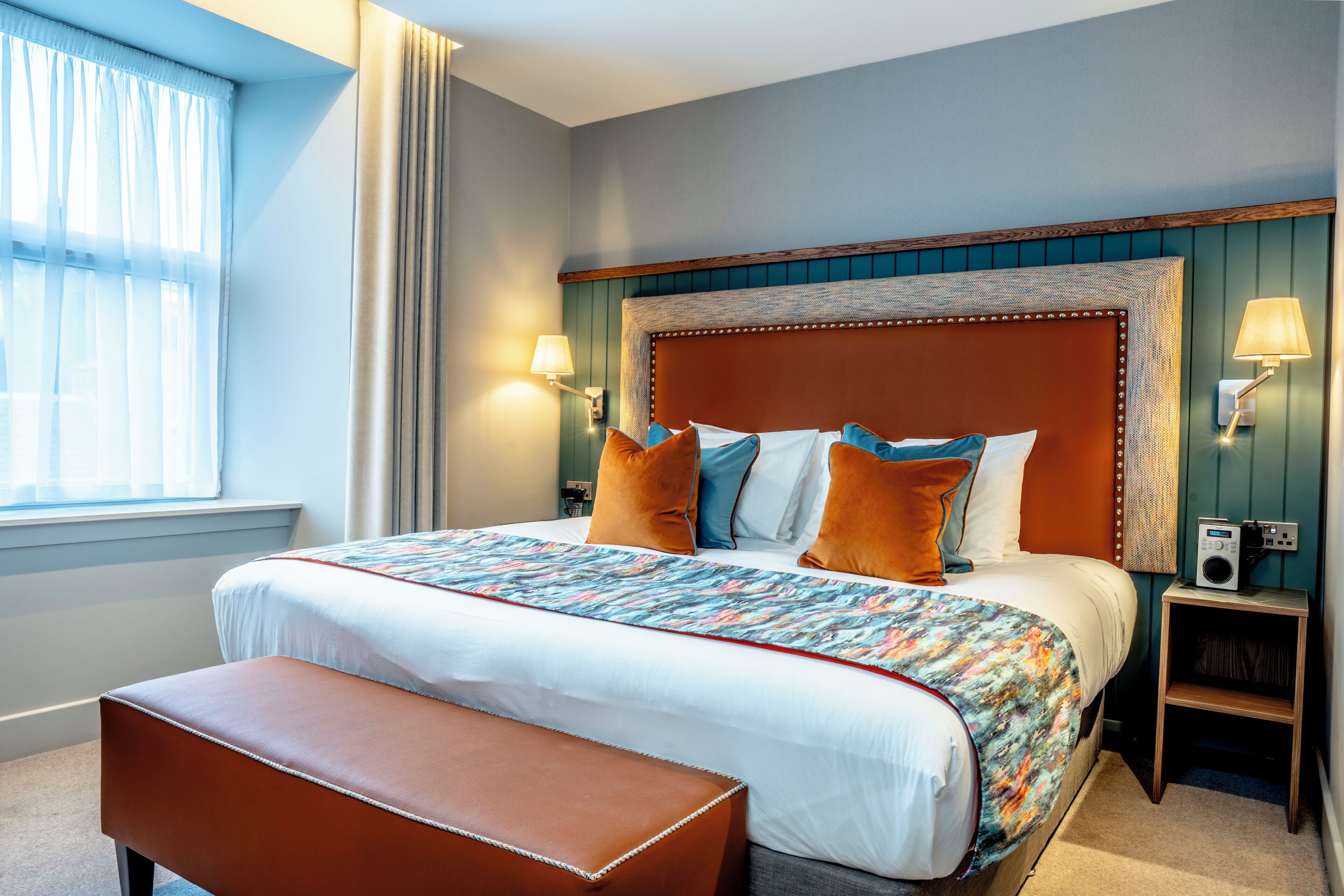 A neatly made bed with a patterned bedspread, a wooden headboard, and two bedside lamps.