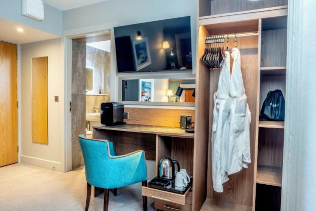 A hotel room with a TV, a desk with a chair, a wardrobe, and a coat rack.