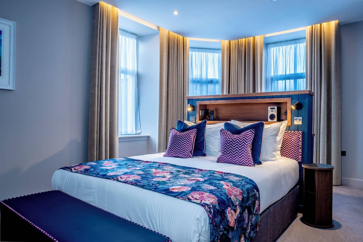 A modern hotel room with a large bed, a wooden headboard, and a bedside table.