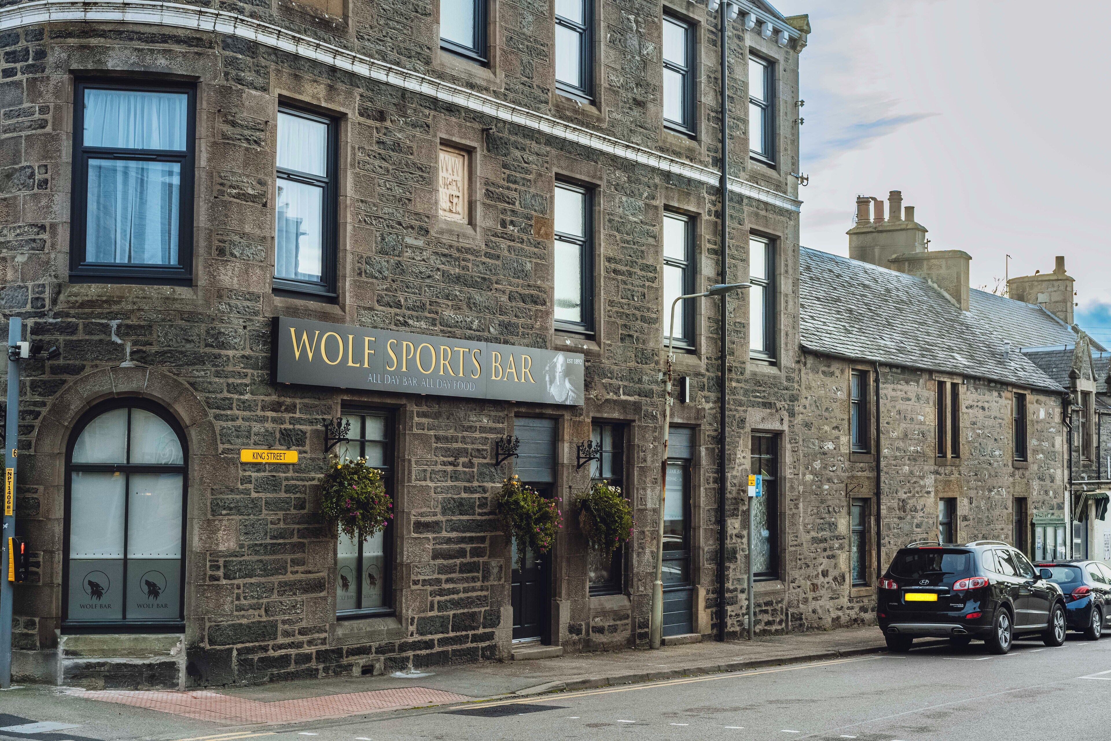 A stone building with a sign reading "WOLF SPORTS BAR".