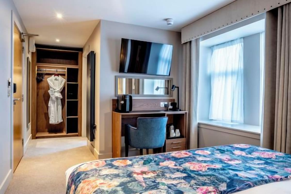 Ett hotellrum med en säng, ett skrivbord, en tv, en garderob och ett fönster med gardiner.