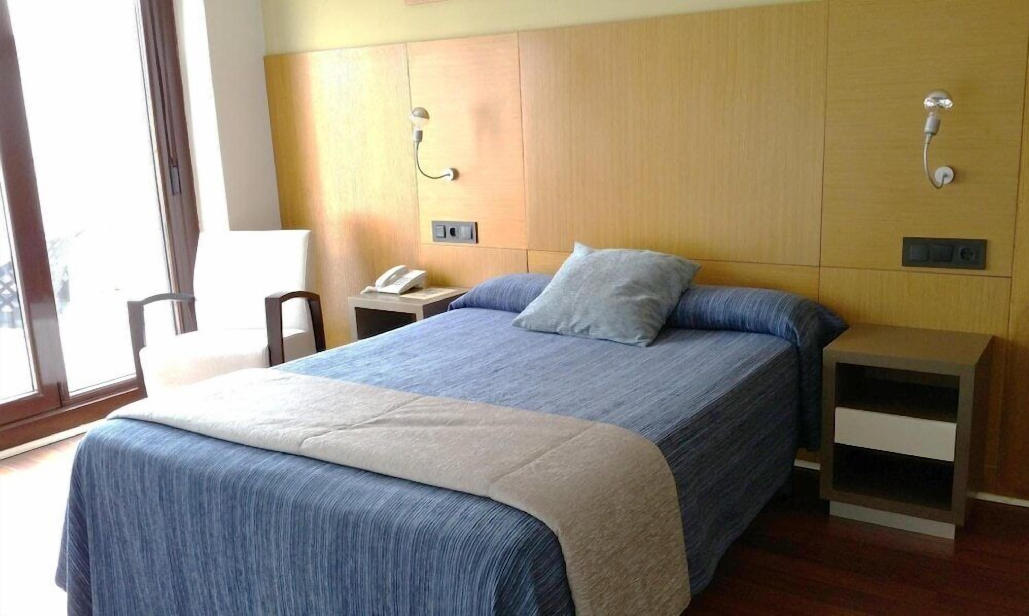 Een hotelkamer met een bed, nachtkastje, stoel en een telefoon aan de muur.