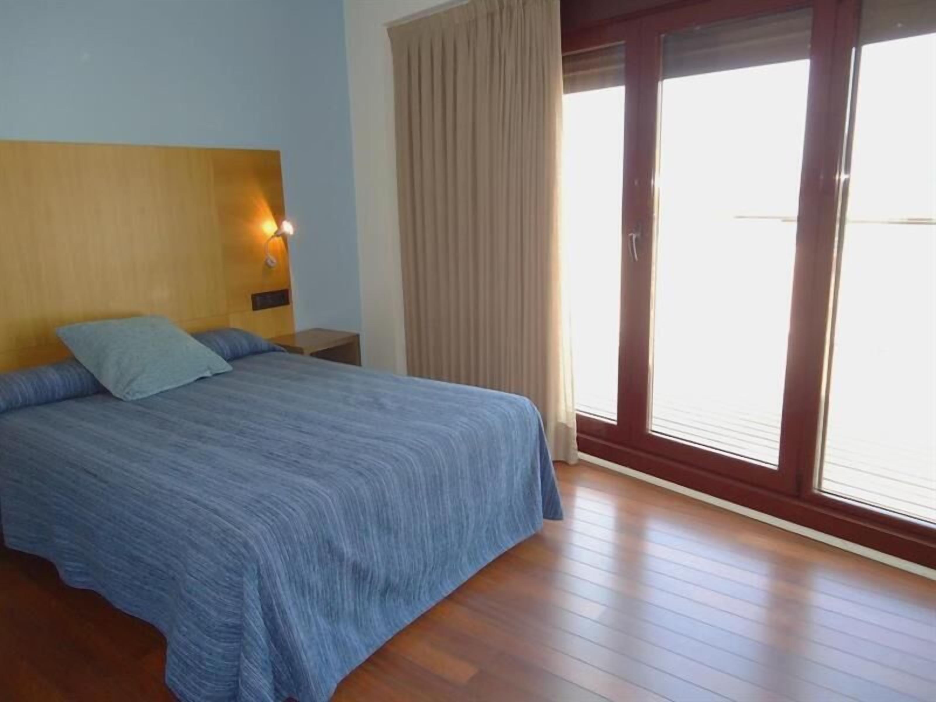 A bedroom with a bed, a nightstand, a wall-mounted lamp, and a sliding glass door to the outside.