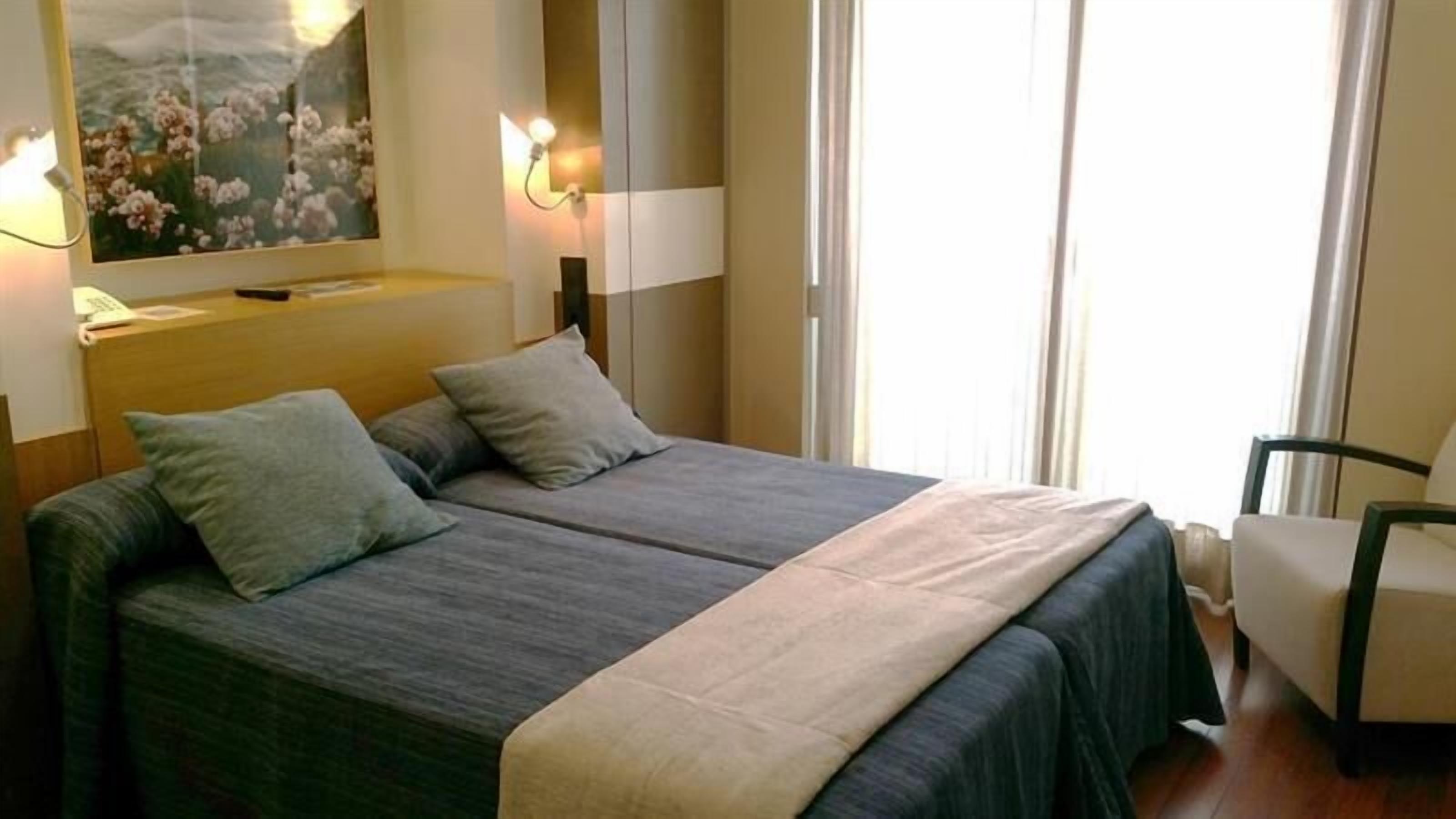 Un llit de matrimoni amb dos coixins, una tauleta de nit, una làmpada, un quadre i una cadira.