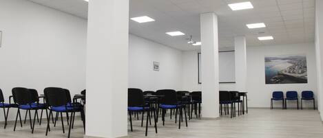 A conference room with rows of chairs, white walls, and a large window with a view of a bridge.