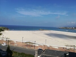Una playa con una vista despejada del océano, un área de estacionamiento con una señal de stop, y una carretera en primer plano.