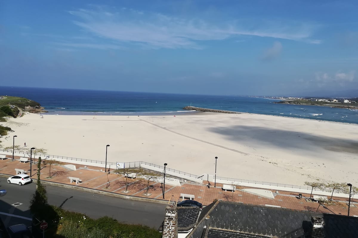 A beach with a paved walkway and benches, a stop sign, and a road with a white car.