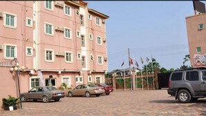 A multi-story building with a pink facade, a parking area with several cars, and a flagpole with multiple flags. - Keviz Hotel (Lagos)