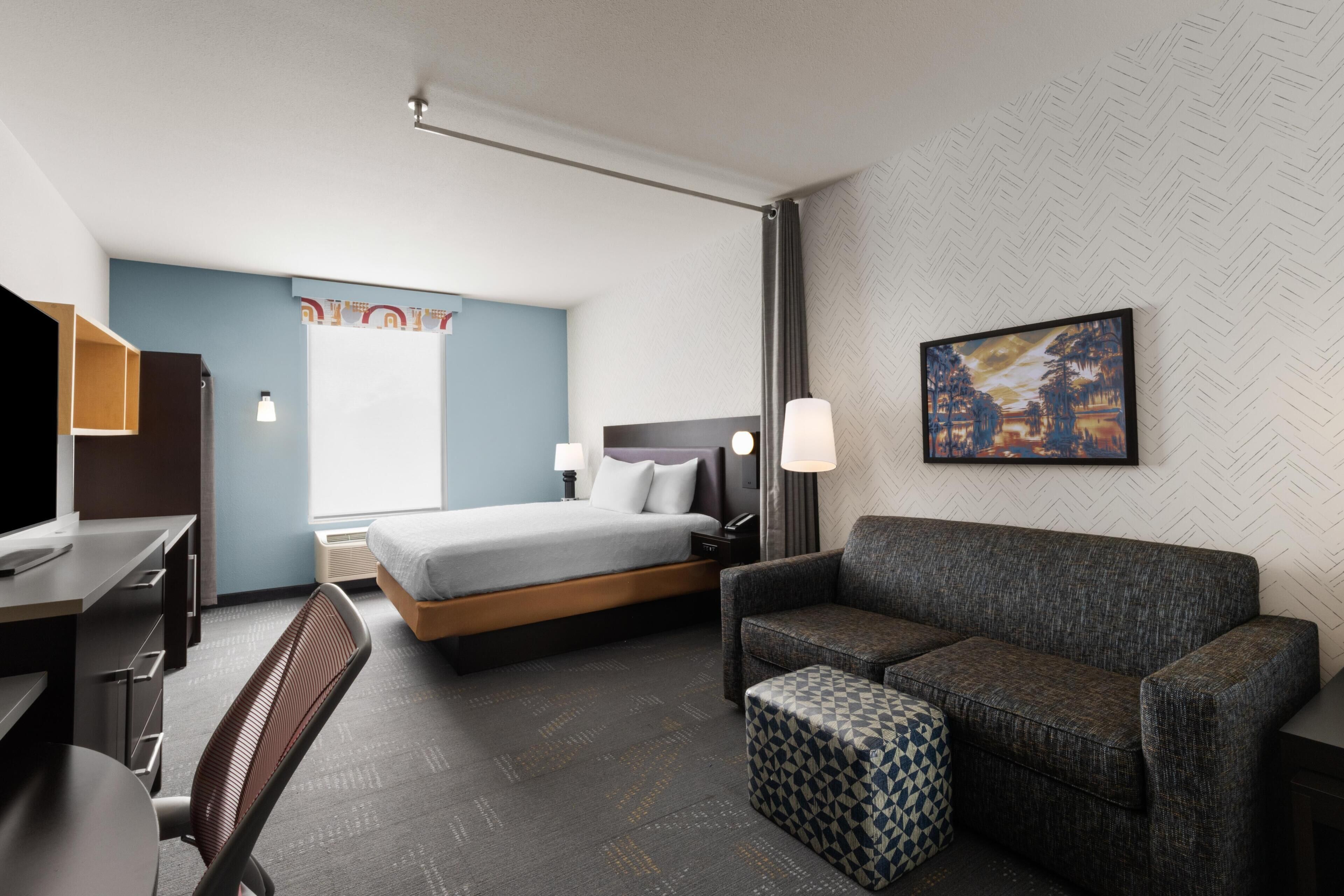 A hotel room with a bed, a desk, a chair, a sofa, and a small ottoman.