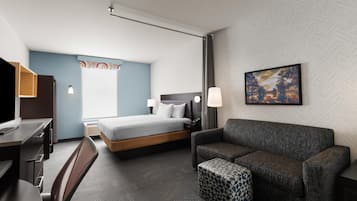 A hotel room with a bed, a desk, a chair, a sofa, and a small ottoman.
