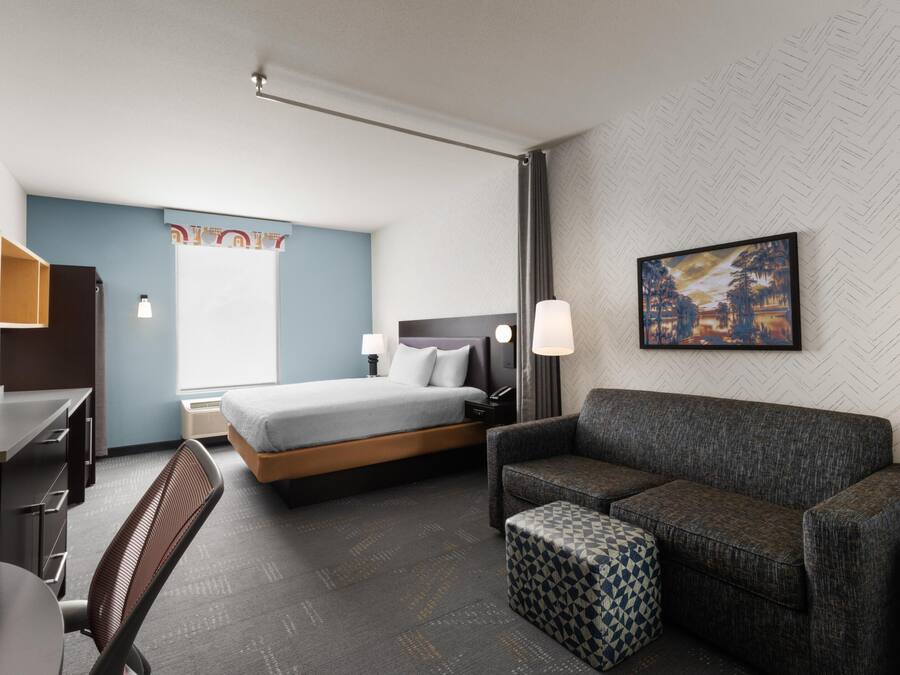A hotel room with a bed, a desk, a chair, a sofa, and a small ottoman.