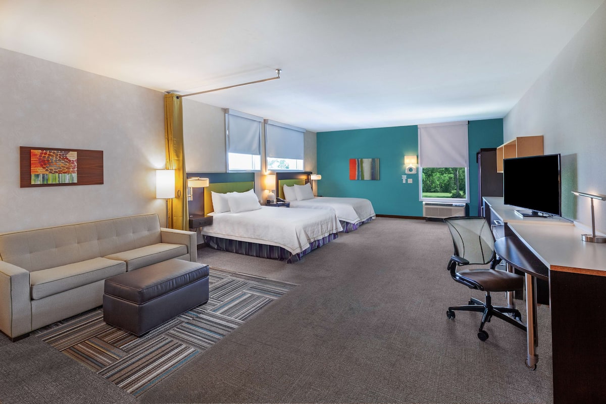 Une chambre d’hôtel avec un canapé, deux lits, un bureau, une chaise et un téléviseur.