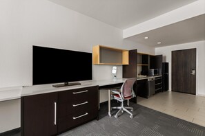 Un espacio de oficina moderno con una gran televisión de pantalla plana, un escritorio, una silla, un microondas y un refrigerador.