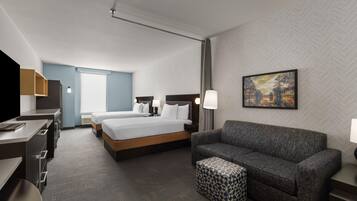 A hotel room with a bed, a sofa, a TV, and a painting on the wall.