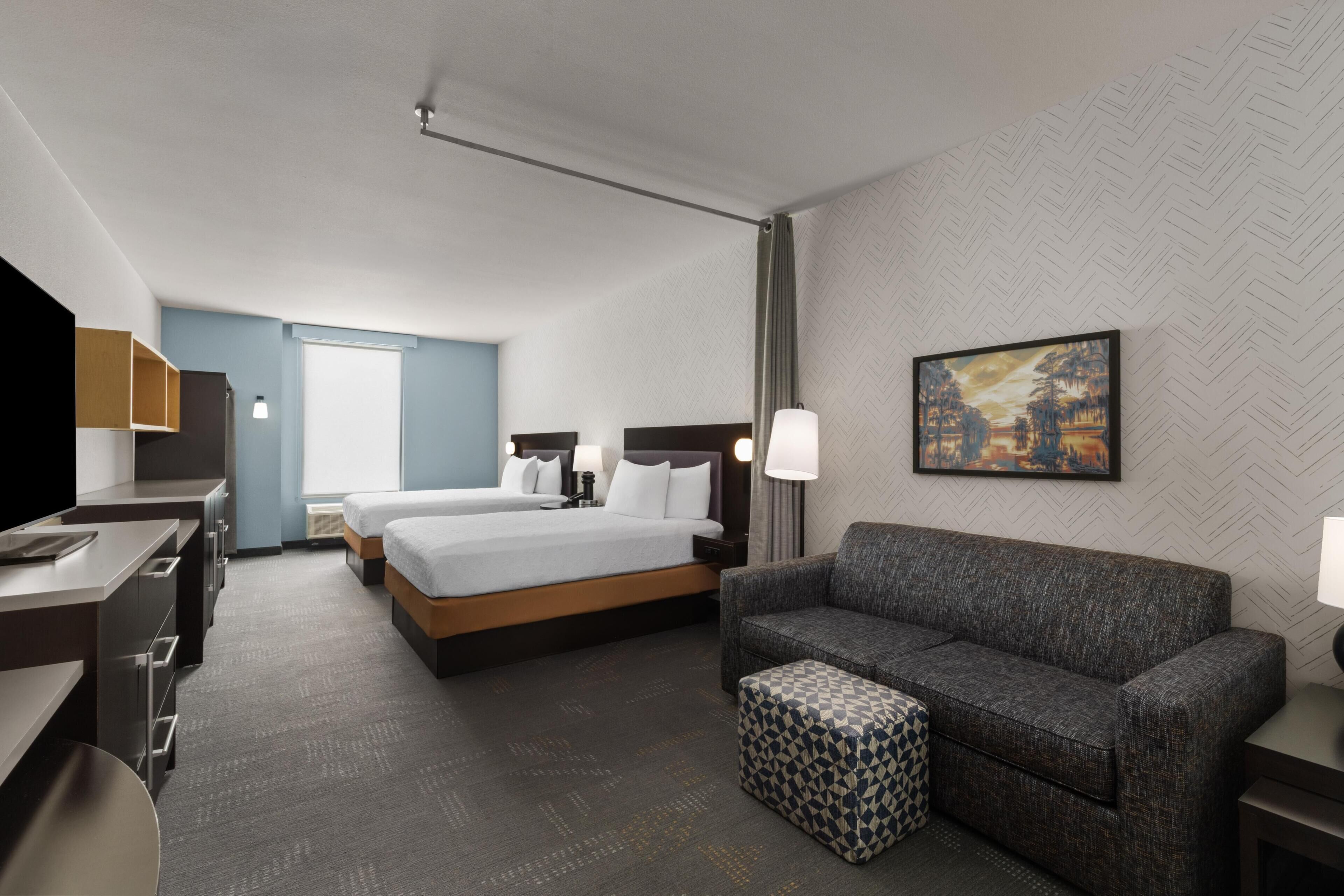 A hotel room with a bed, a sofa, a TV, and a painting on the wall.