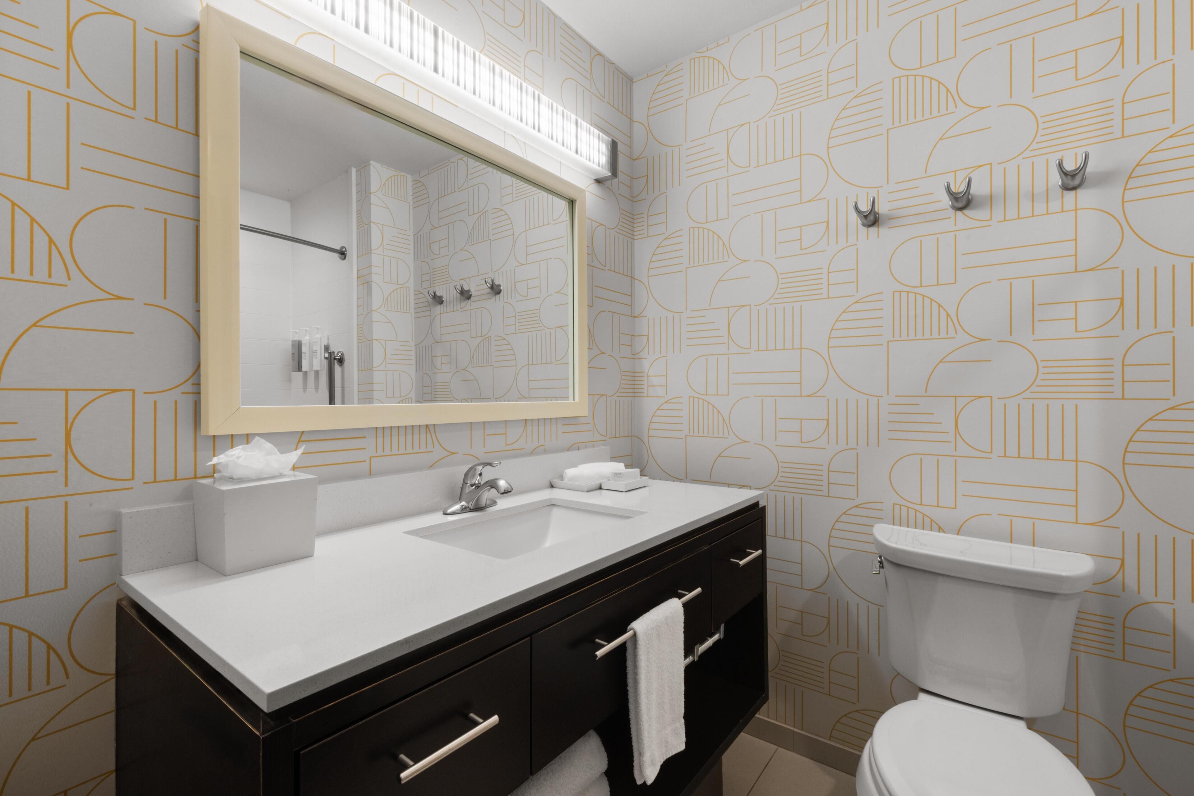 Een moderne badkamer met een grote spiegel, een witte wastafel, een zwart aanrecht en een toilet.