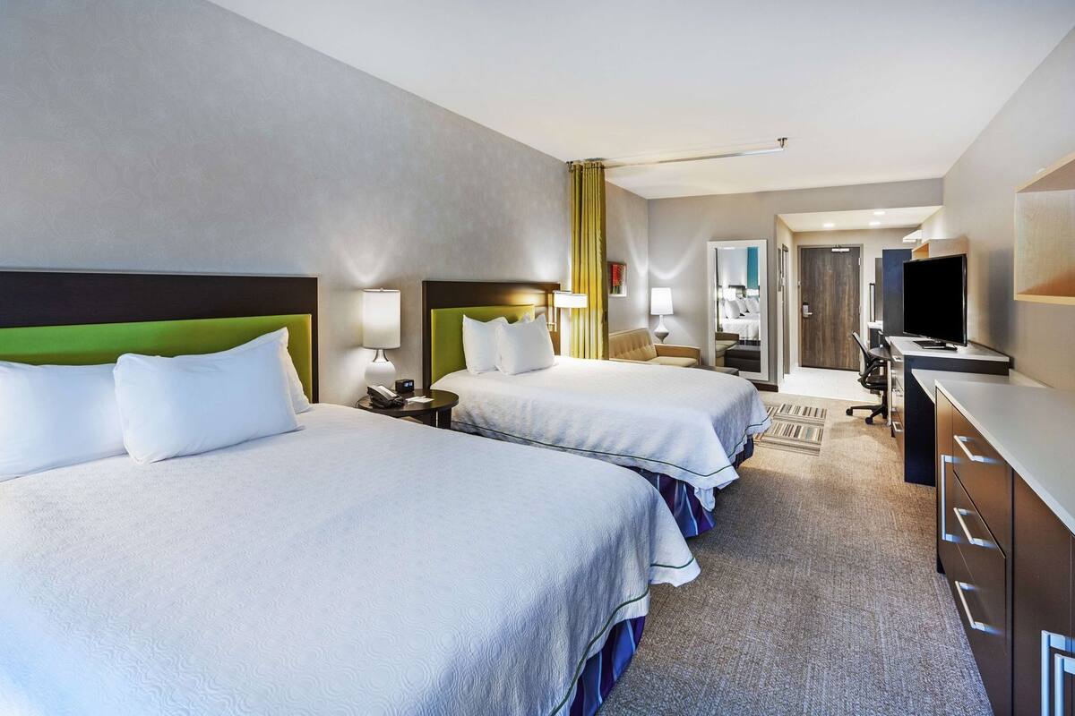 Een hotelkamer met twee bedden, een bureau, een televisie en een badkamer in de achtergrond.