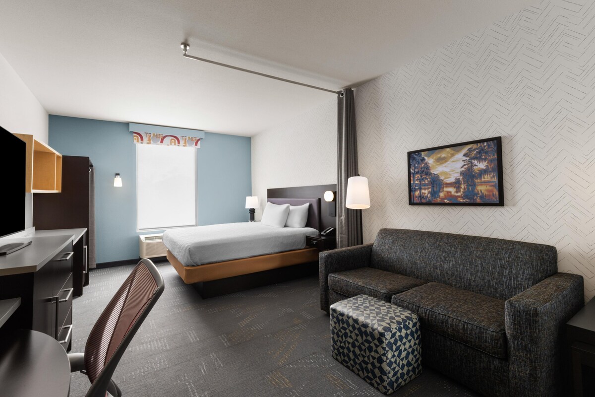 Una habitación de hotel con cama, escritorio, silla, sofá y un pequeño otoman.