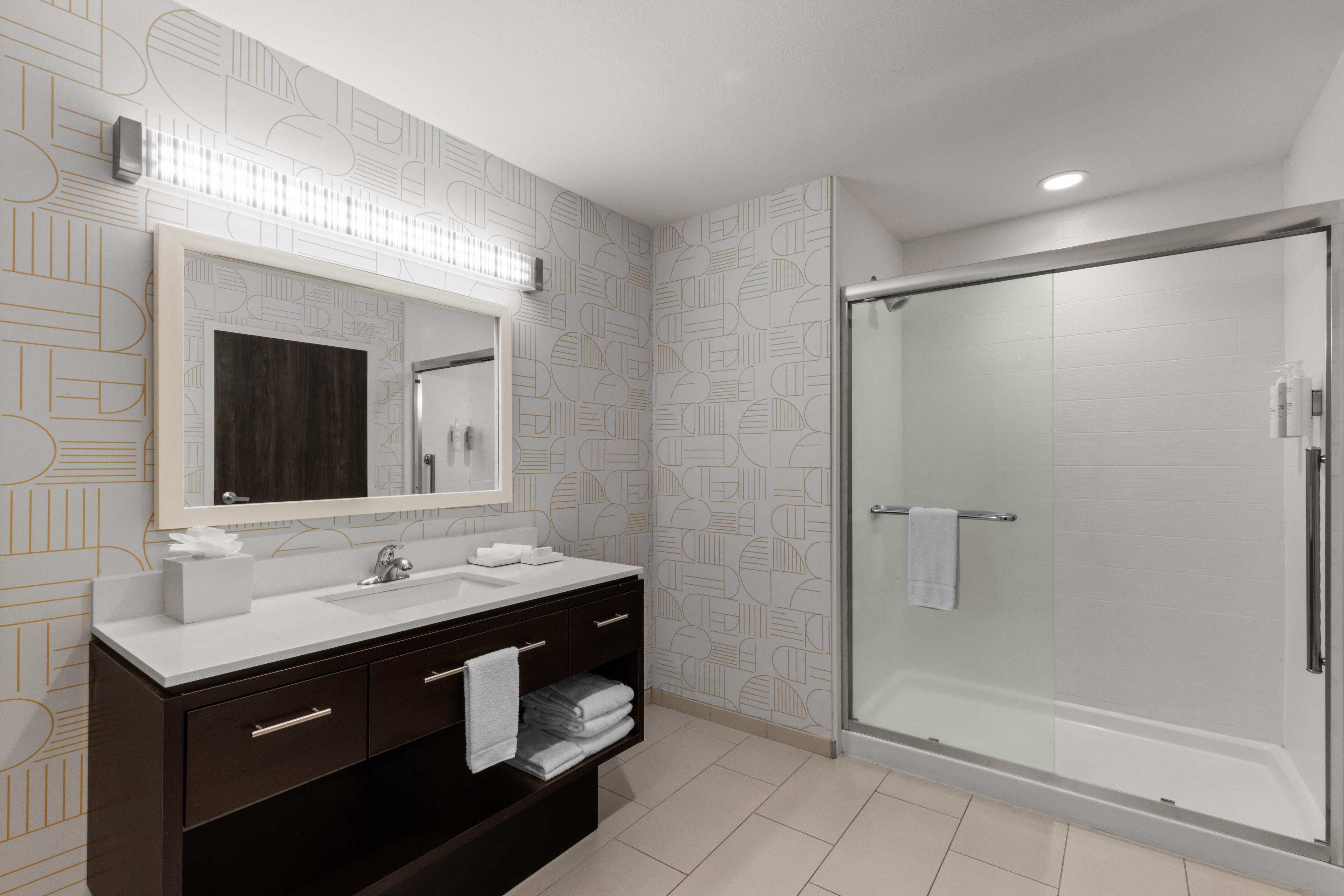 A modern bathroom with a large mirror, a sink, a dark vanity, and a glass-enclosed shower.