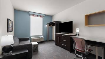 A hotel room with a bed, a desk, a chair, a TV, a lamp, and a window with curtains.
