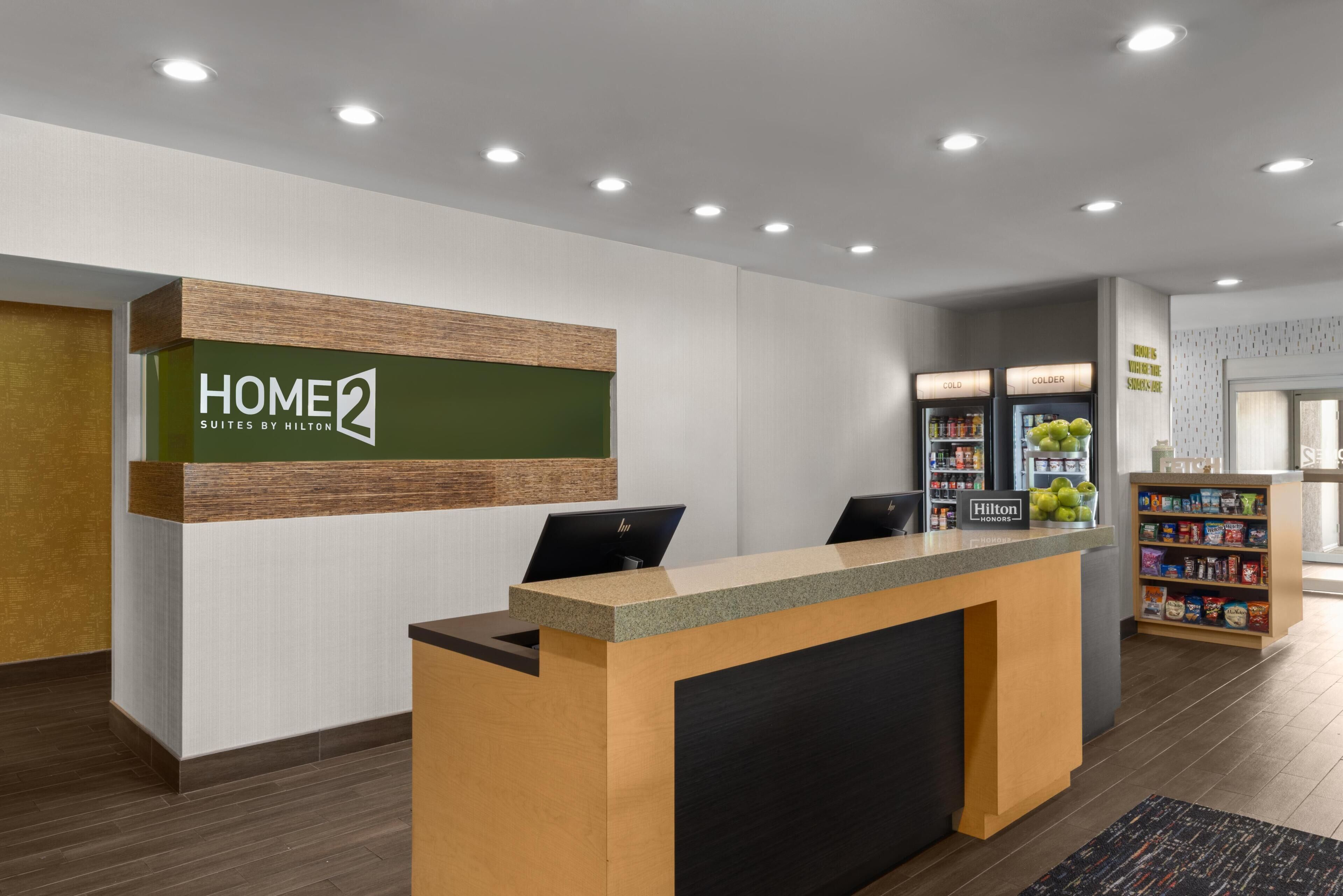 A hotel reception desk with a sign reading 'HOME 2 SUITES BY HILTON' and a computer monitor.