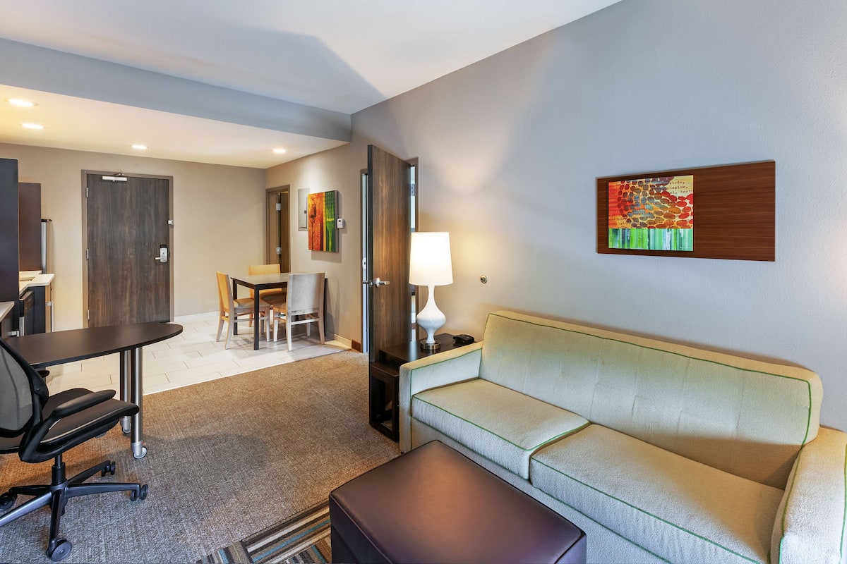 Une chambre d’hôtel avec un canapé, un bureau et une chaise. Une lampe se trouve sur une table d’appoint.