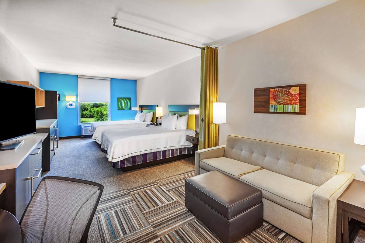Une chambre d’hôtel équipée d’un lit, d’un canapé, d’un bureau, d’une télévision et d’une fenêtre donnant sur un paysage verdoyant.